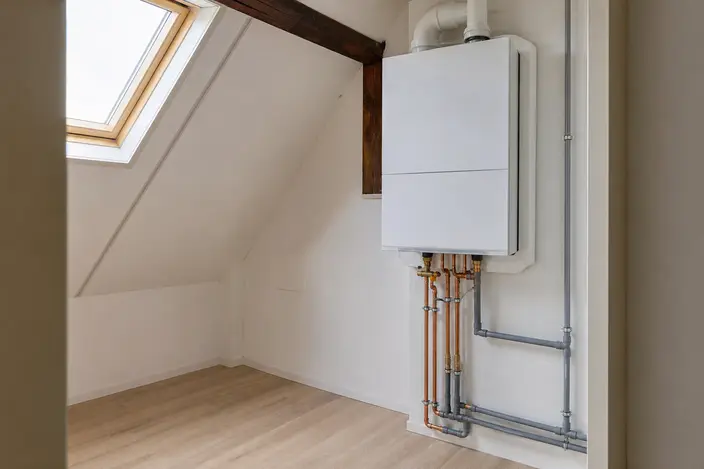 AI-beeld: een witte cv-ketel zonder merk aan de muur van een zolder, met leidingen eronder